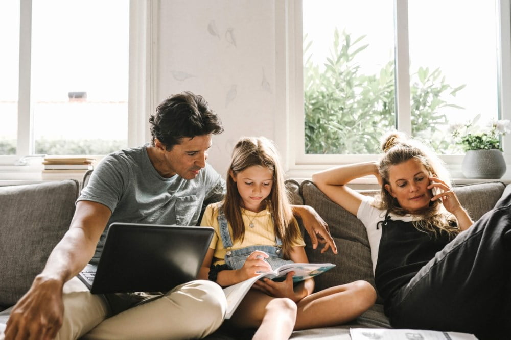 Familie i sofaen med pc, nettbrett og blader