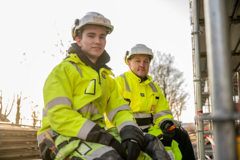 To sittende byggearbeidere i gul dress og hjelm